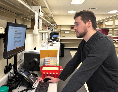 A man standing at a computer with shelves behind him