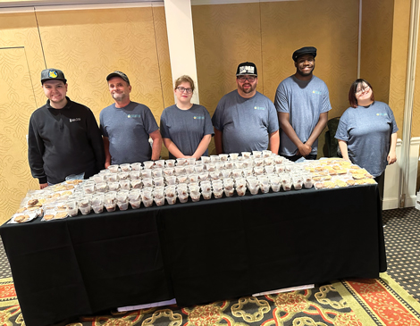 serve-article a group of people in matching tshirts standing behind a table full of food samples