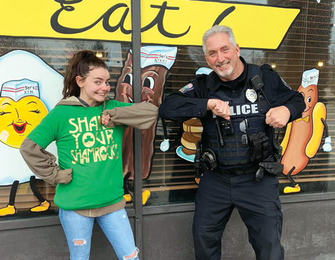 A woman in a green shirt smiling and bumping elbows with a police officer