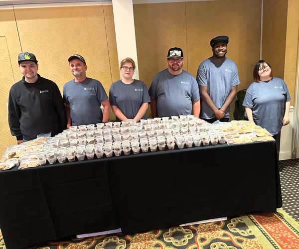 a group of people in matching tshirts standing behind a table full of food samples