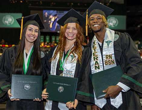 Three people in graduation caps and gowns, holding their Cleveland State University diplomas