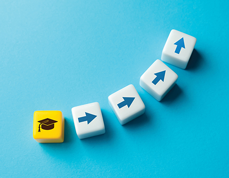 feb25-column-article A yellow dice with a black graduation hat on it, followed by 4 white dice with arrows moving in a line upward