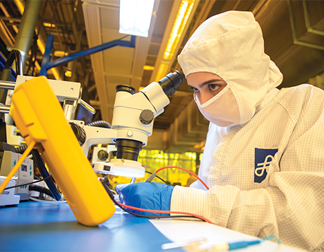 A student in protective gear looking through a microscope 