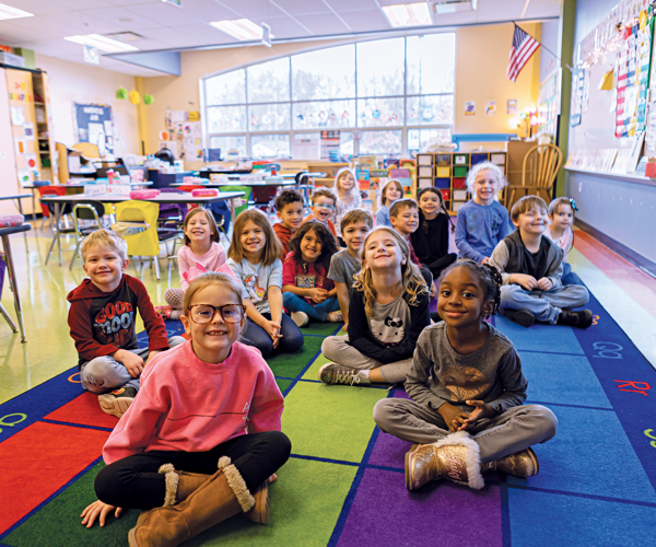 a group of young students sitting on a colorful carpet and smiling