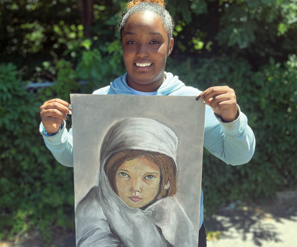 A young woman holding up a piece of her artwork