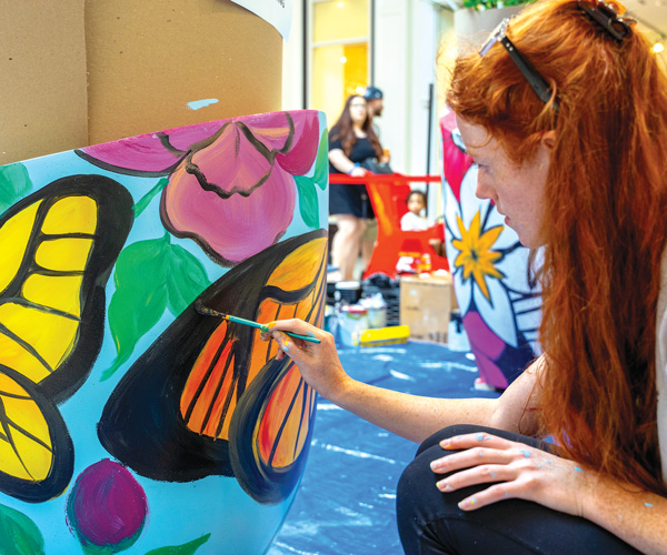 a woman with long red hair painting a colorful butterfly