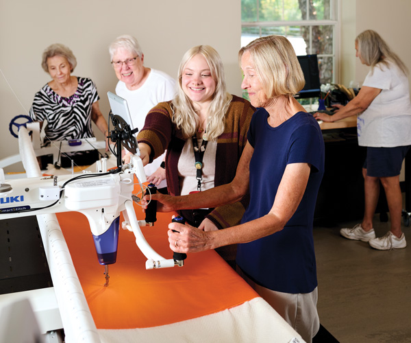 A group of women gathered around a long-arm sewing machine