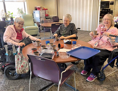 three women gathered around a table, holding seed pots and smiling