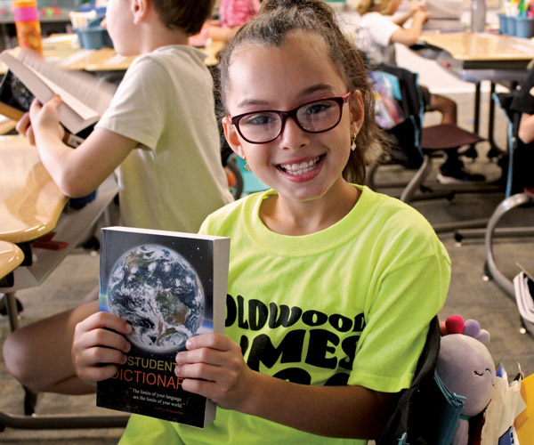 A young student smiles and holds up a dictionary
