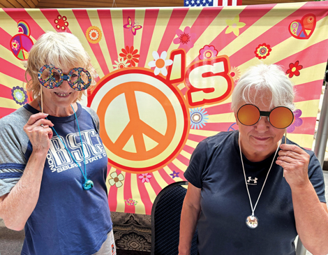rocky-river-senior-center-party-article Two women standing in front of a 1970s groovy background and holding funky glasses in front of their faces