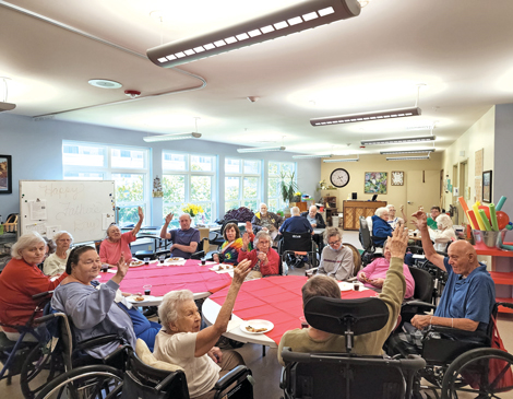 A group of seniors gathered around a few tables, waving