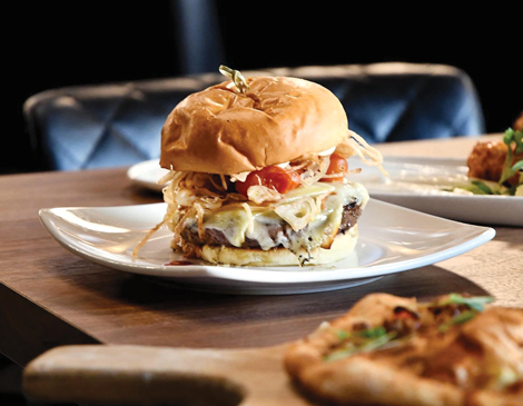 a burger on a white plate sitting on a wooden table