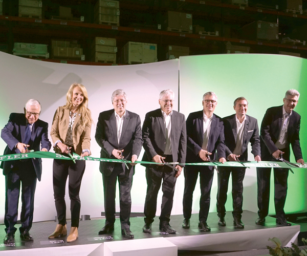 A group of business people smiling and cutting a long green ribbon