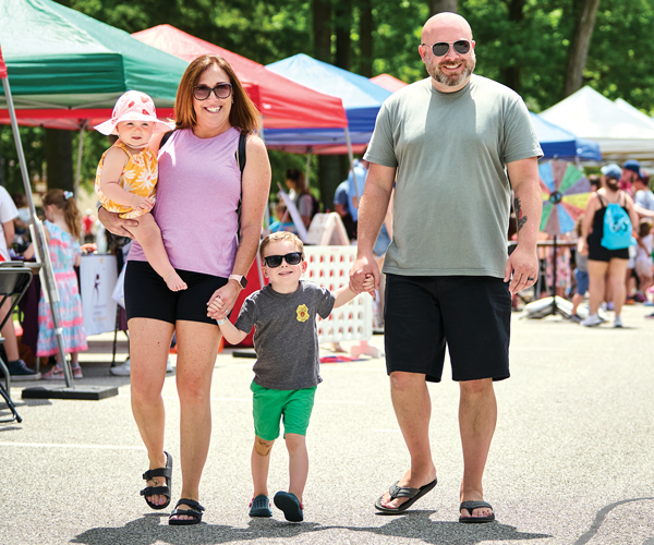 A family of four holding hands and smiling while they walk toward the camera