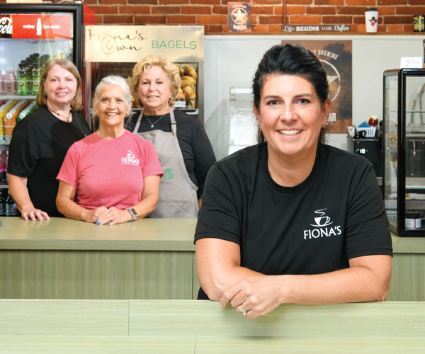 Megan Wickline smiling in Fiona's Coffee Bar and Bakery with a group of her employees smiling behind her